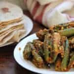 Stuffed Okra in a white platter with Indian roti's on the side in a white plate.