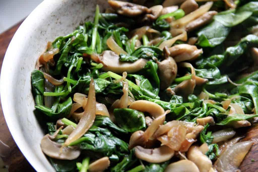 sauteed onions, mushrooms and baby spinach in a pan 