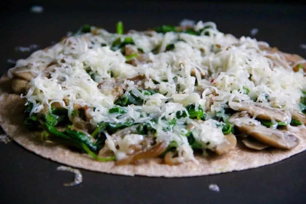 cheese topped on a tortilla over spinach and mushroom filling 