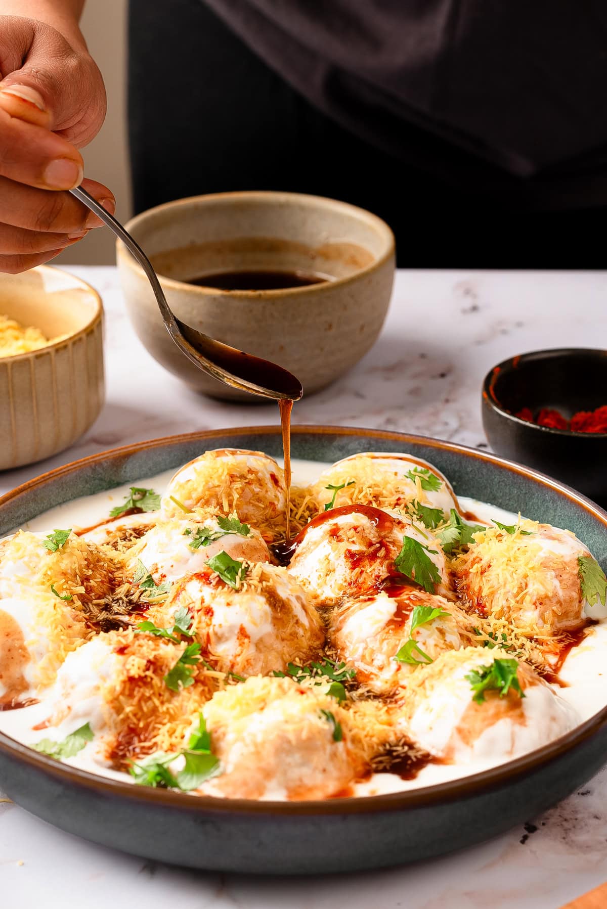 drizzling tamarind chutney over dahi vada