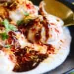 Dahivada with yogurt garnished with tamarind-date chutney, red chili powder and cilantro in a black plate