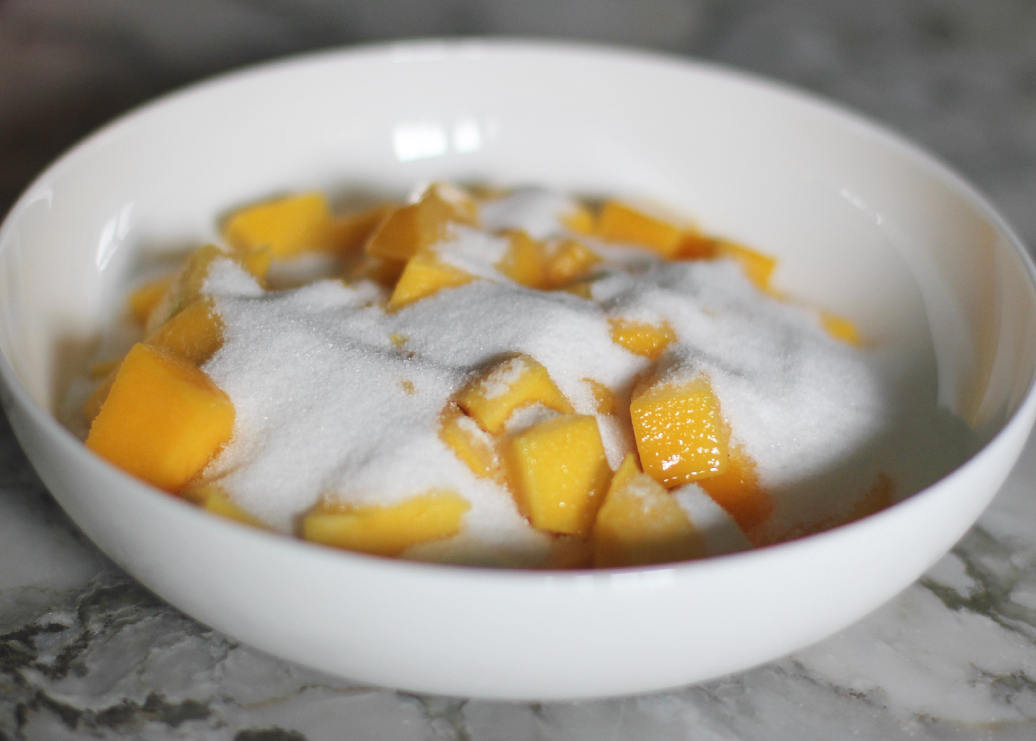 cut up mango with sugar in a white bowl