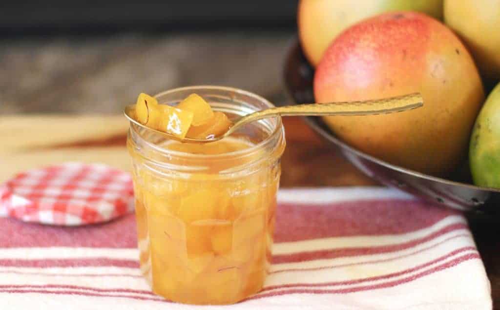 Raw Mango Jam in glass jar with spoon on striped dish towel