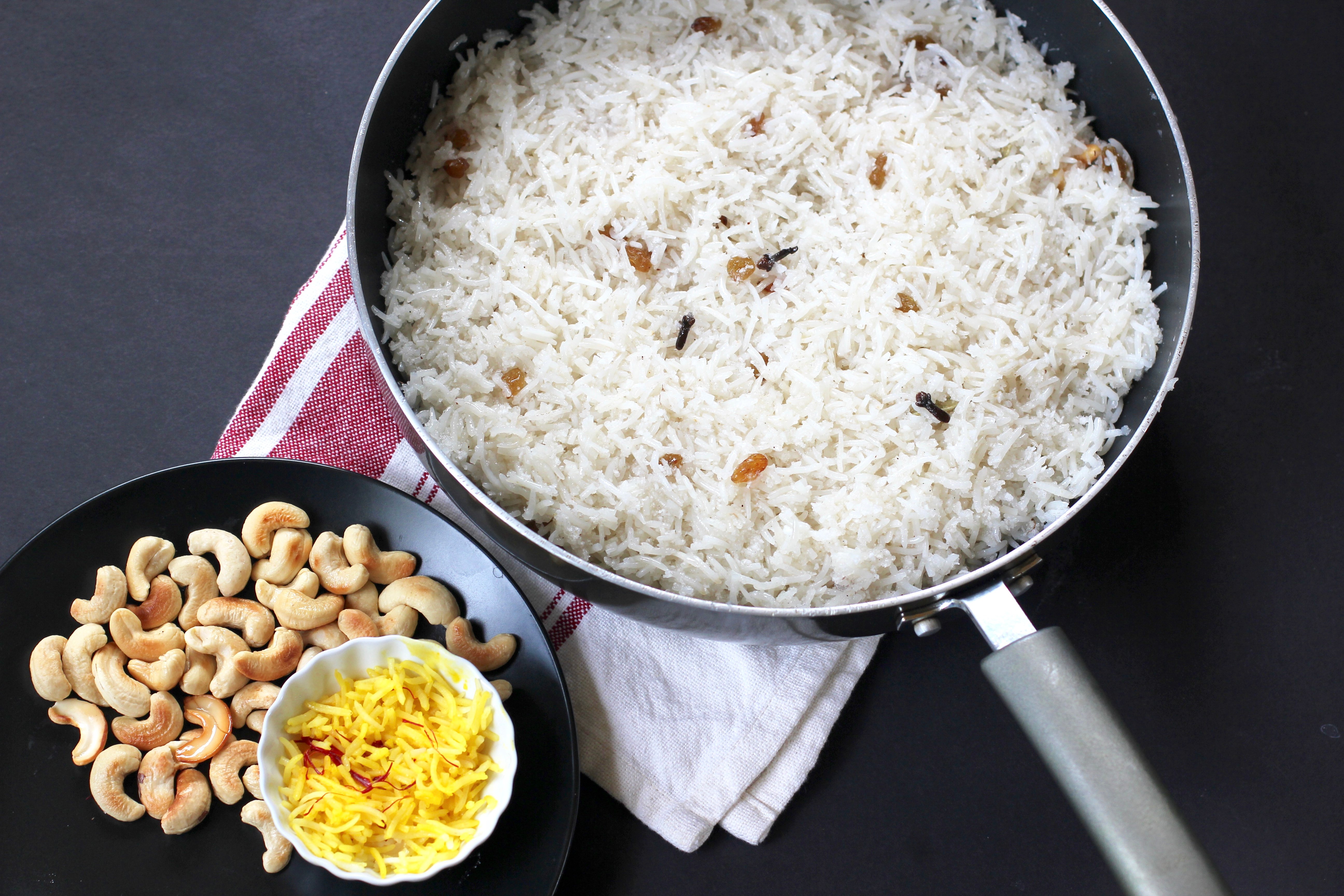 coconut rice in a non stick pan with cashews and bloomed saffron next to it. 