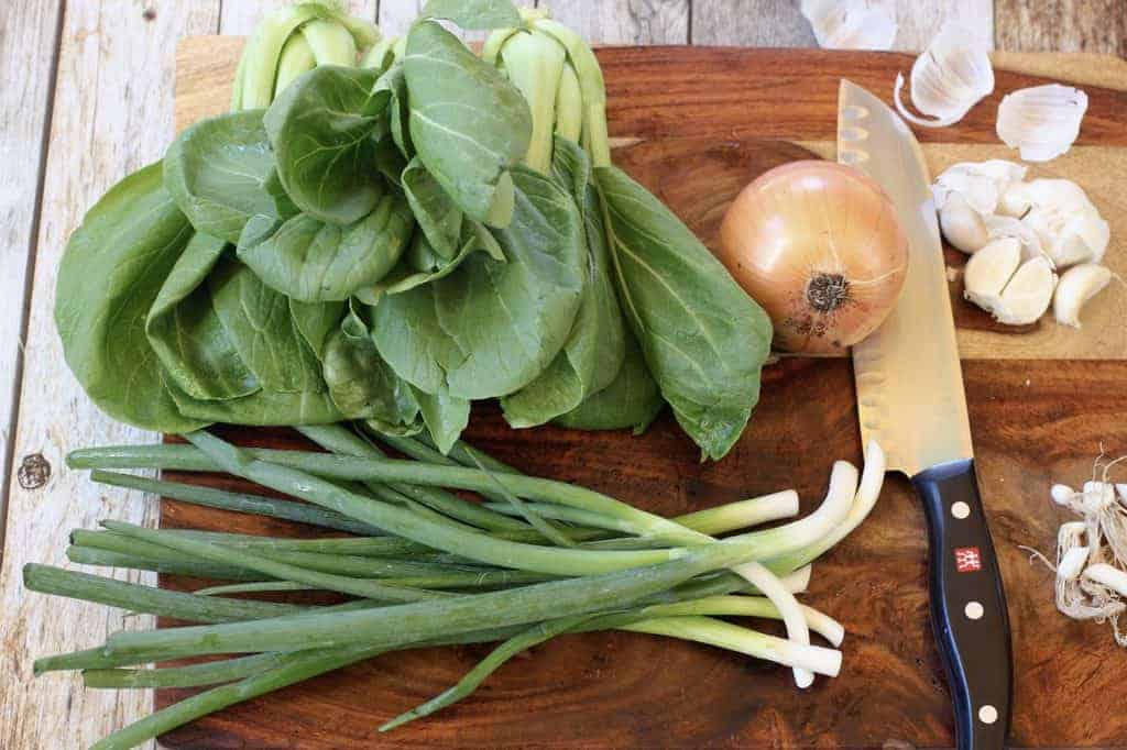 bok choy, scallions, onion and garlic on a cutting board 