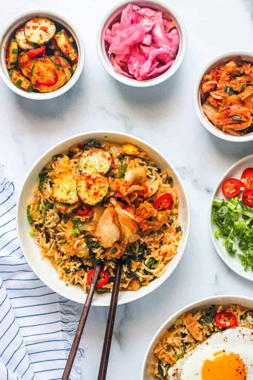 kimchi fried rice in white bowl with chop sticks served with side dishes