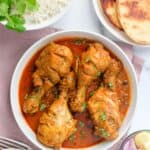 chicken korma in a white bowl with rice and naan on the side