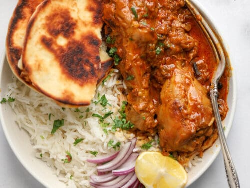chicken korma in s white bowl with rice and naan