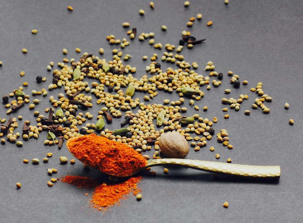 berbere spice blend in a spoon with whole spices on the side 
