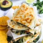 stack of spinach and mushroom quesadiilas with chips, avocado and lime on the side