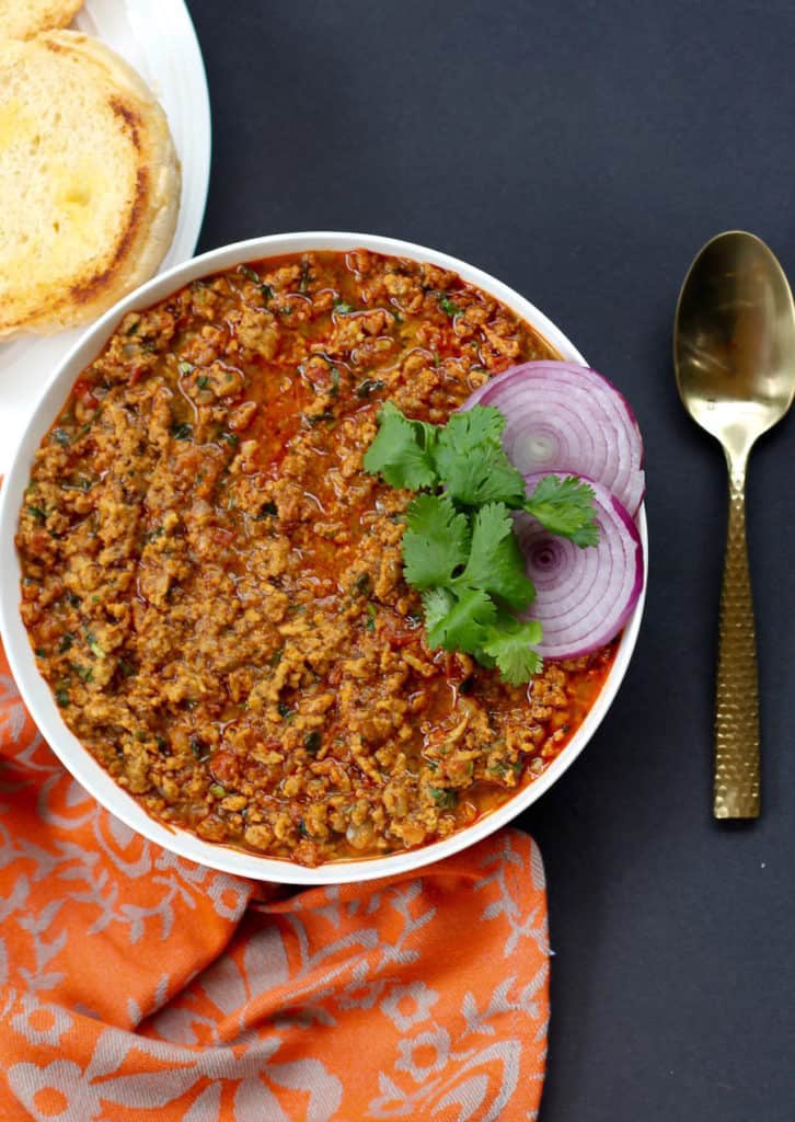 serving bowl with chicken kheema , garnished with cilantro and red onions