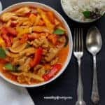 thai red curry chicken with spoon and fork next to it and a bowl of rice