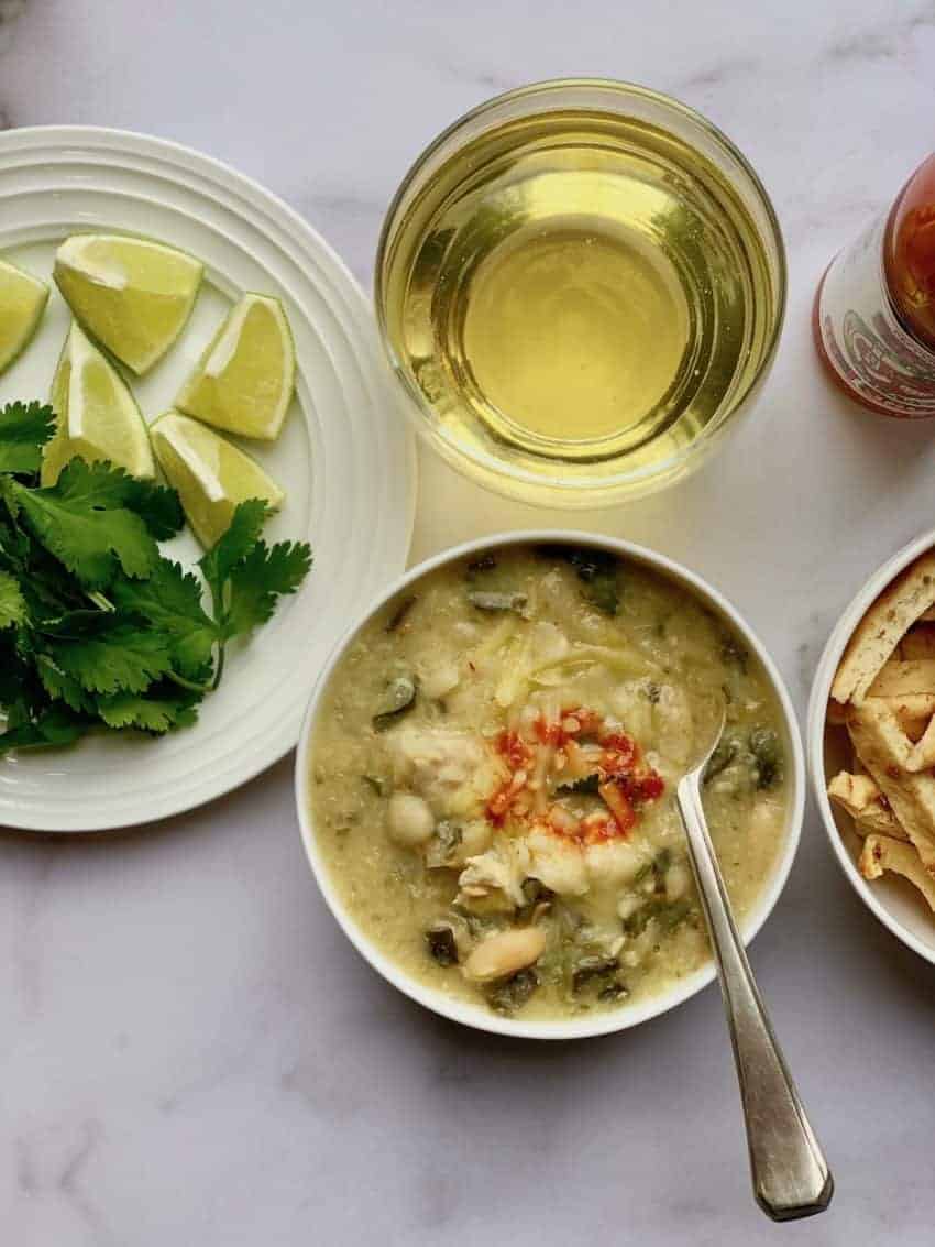 white chicken chili in white bowl with spoon in it with glass of ginger ale