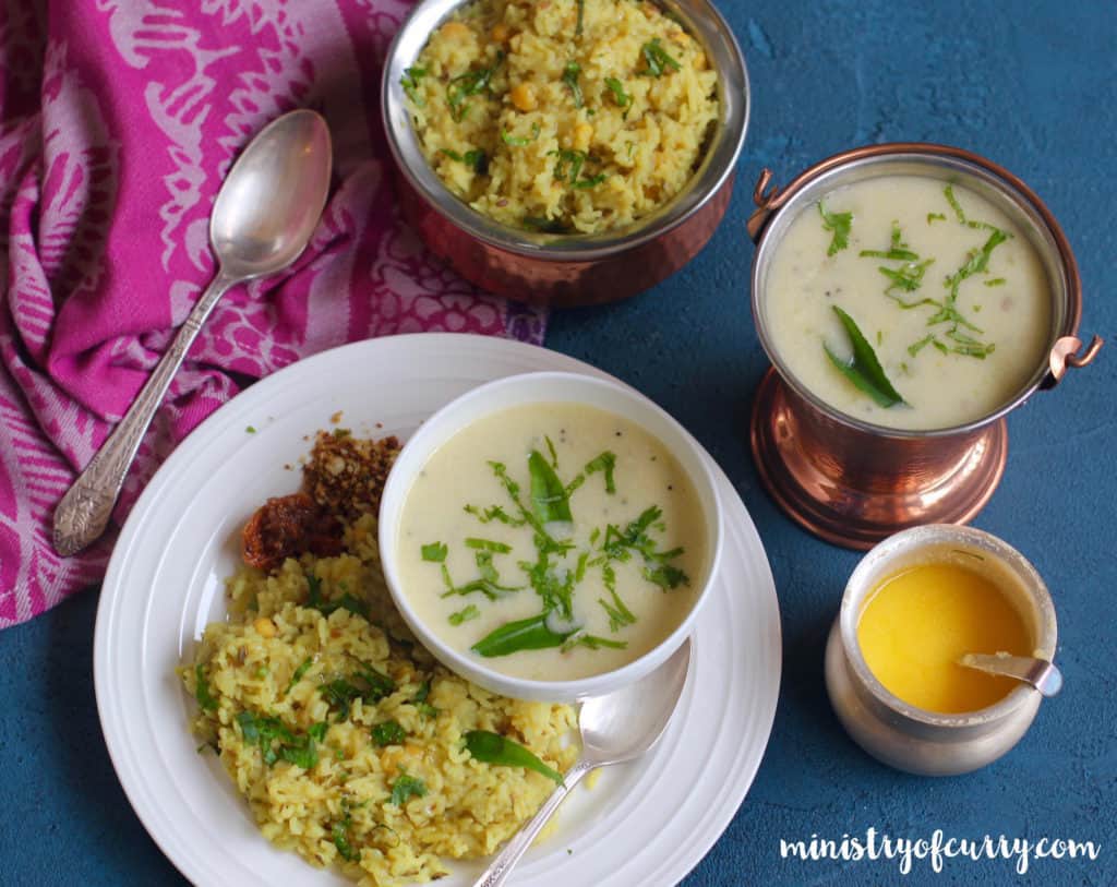 White dinner plate with khichdi and pickle served with a bowl of kadhi.