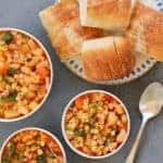 3 white bowls with Pasta e Fagioli soup and a platter of sliced baguette