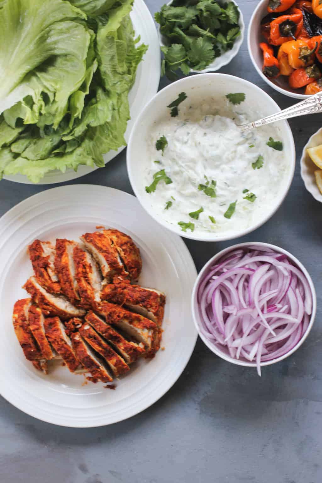 Tandoori Chicken sliced on white platter with bowl of red onion, and raita