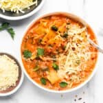 lasagna soup served in a white bowl, garnished with cheese and parsley