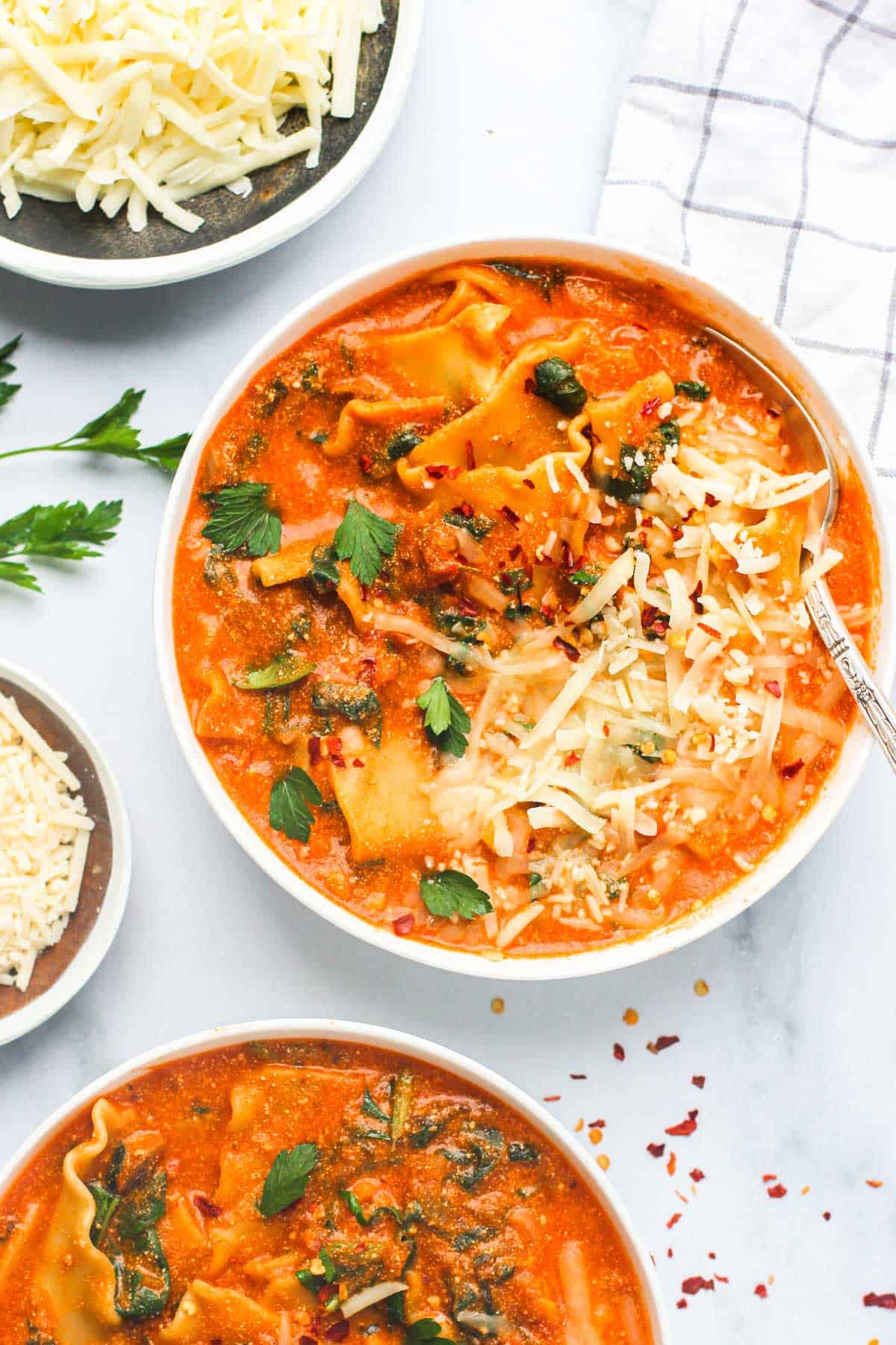 lasagna soup served in a white bowl, garnished with cheese and parsley
