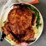 whole tandoori chicken served on a white platter with grilled red onion wedges, chilies, cilantro and lemon wedges.