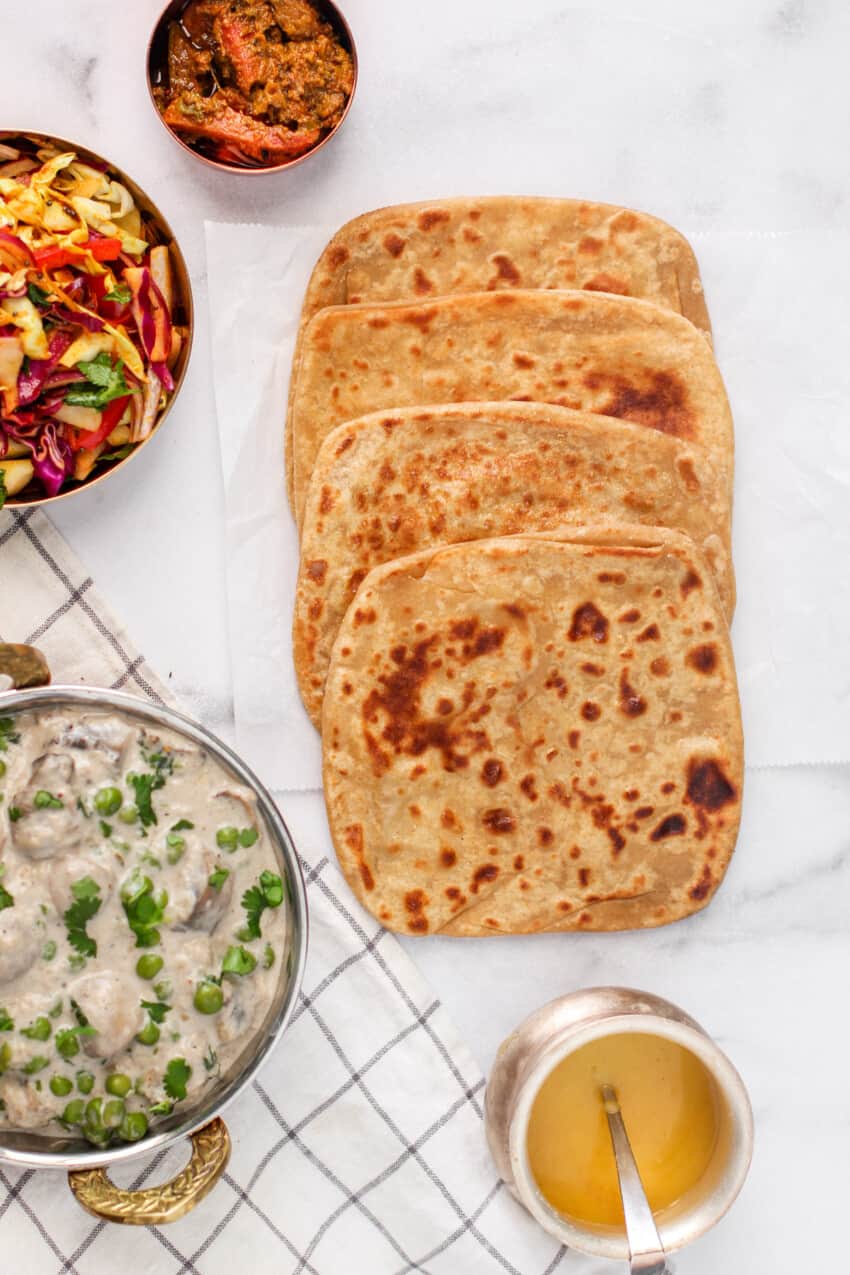 2 square parathas in a platter, 2 triangle parathas in a platter and a silver bowl of ghee