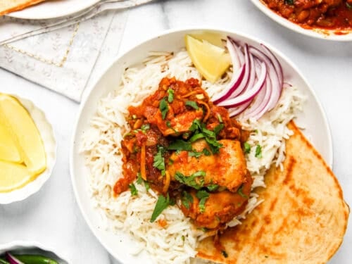 karahi chicken served over basmati rice along with naan, sliced onions and lemon wedge