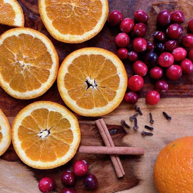Orange slices, fresh cranberries, cinnamon sticks and cloves on a wooden cutting board