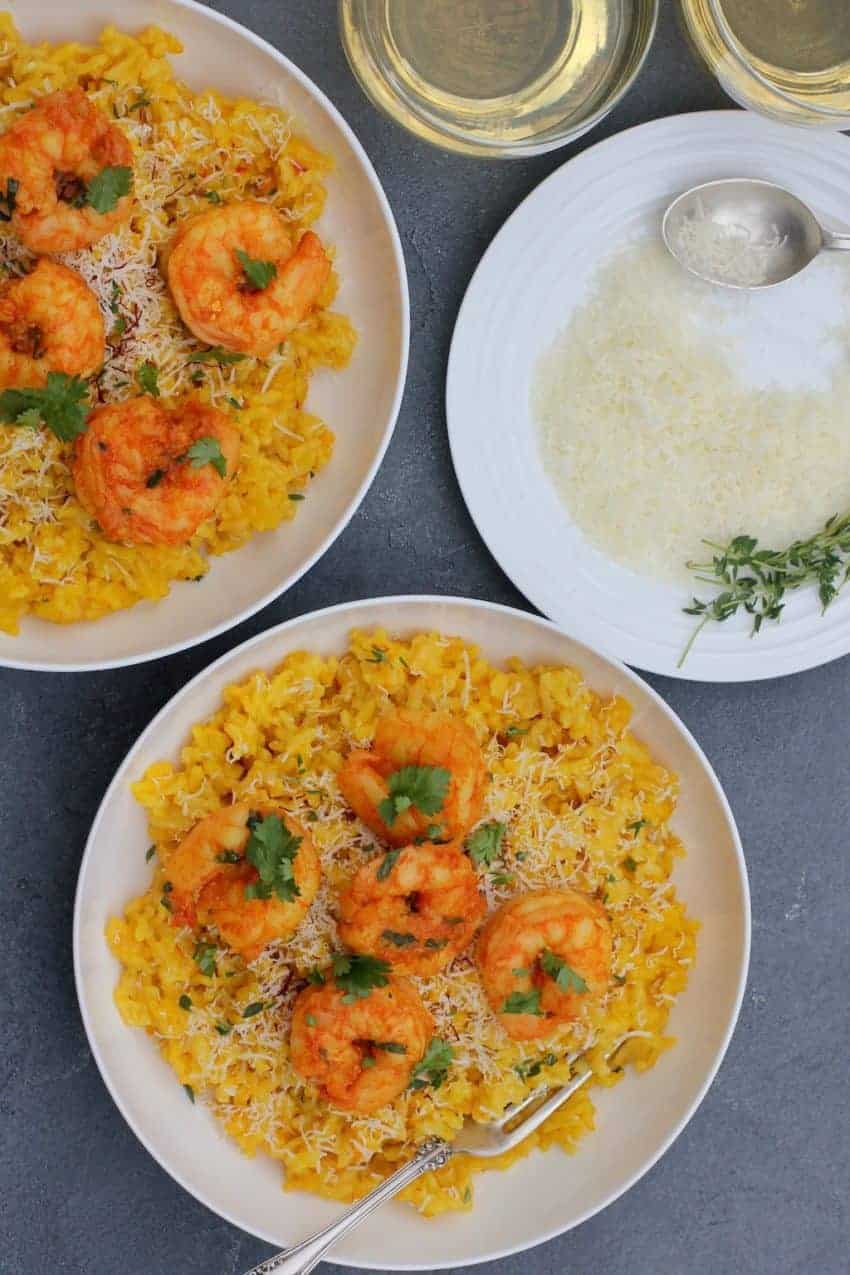Curried Shrimp served over Saffron Risotto, garnished with choppied cilantro served in 2 white bowls. A plate of grated parmesan cheese on the side, with few srings of thyme and a spoon.