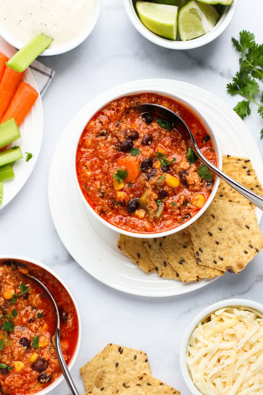 Buffalo chicken chili served in white bowl with spoon with chips on a white plate