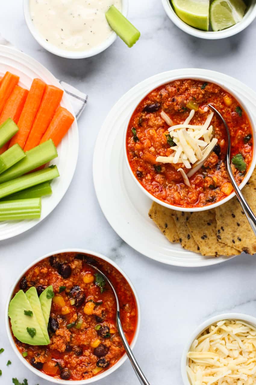 Buffalo chicken chili in white bowl with spoon served with chips on a white plate
