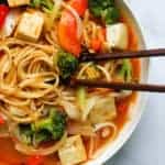 coconut curry noodle soup in a white bowl with chopsticks in the soup.