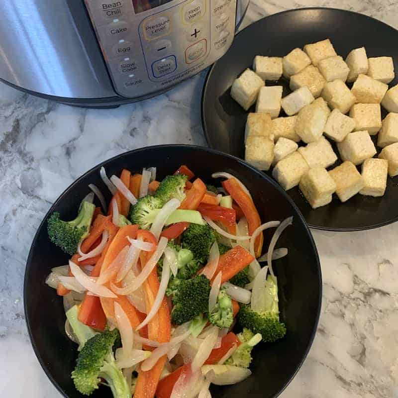 stir fried veggies in a balck bowl, tofu in a black plate with the Instant Pot in the background