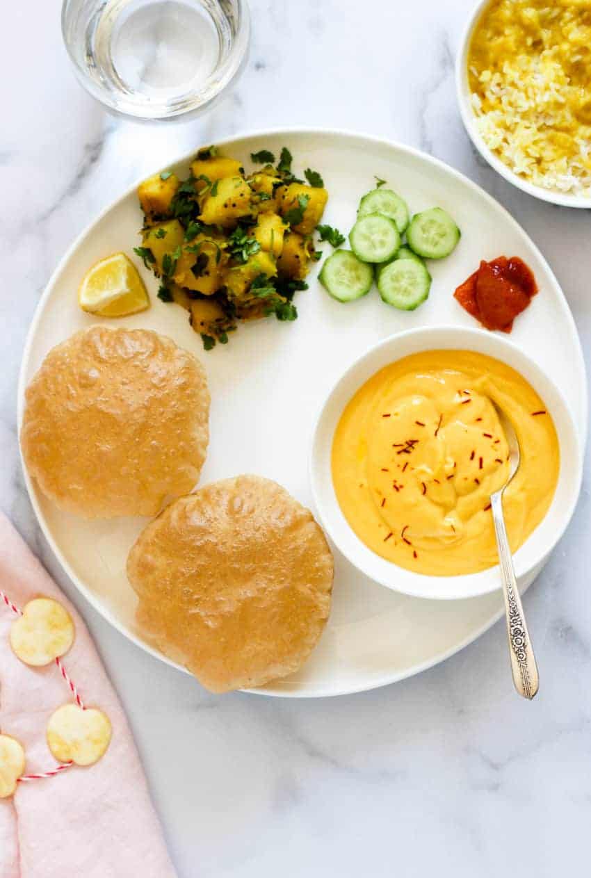 Dinner plate with mago shrikhand, puri;s and batat bhaji