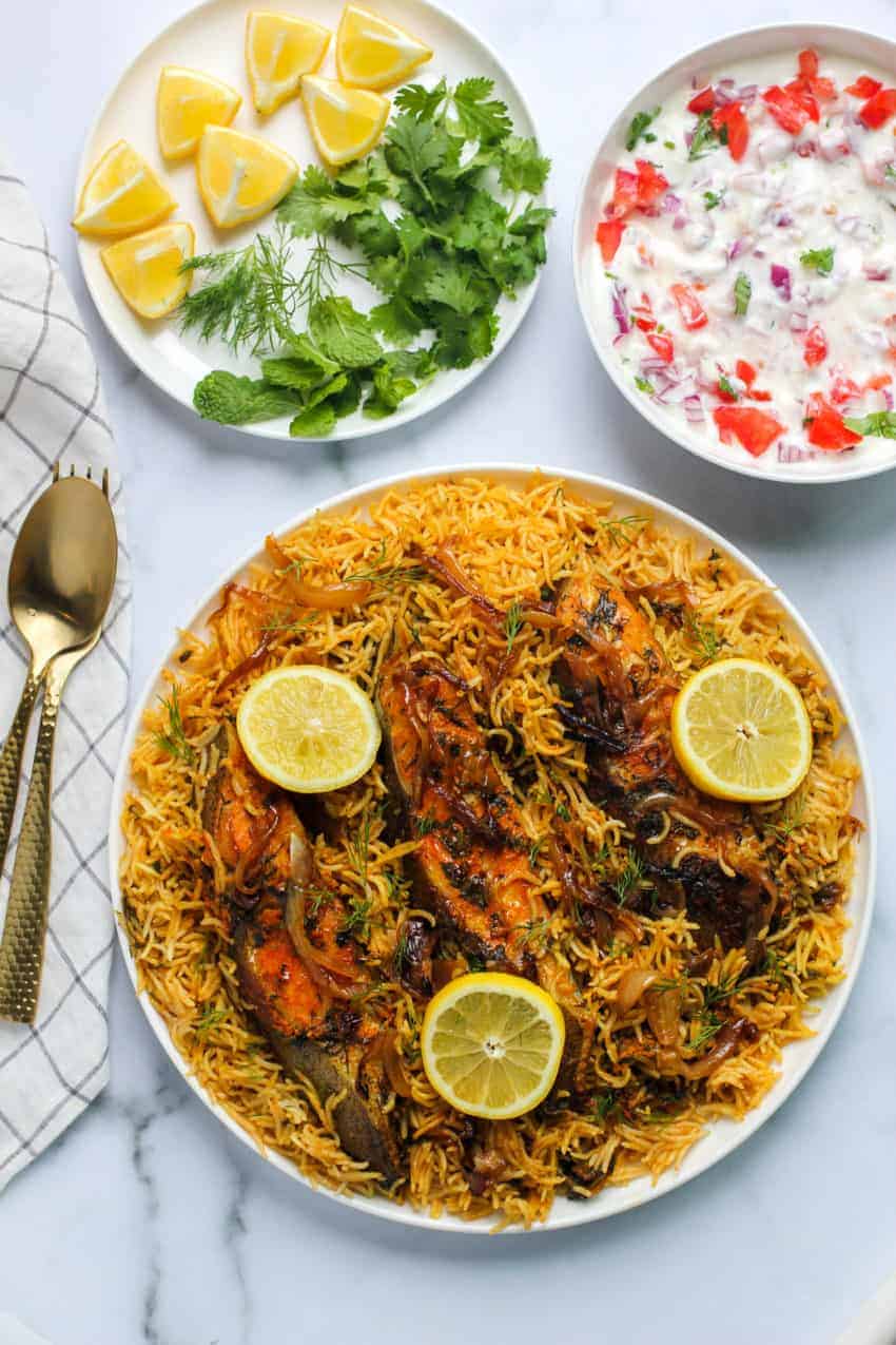 Fish Biryani with lemon slices, raita and garnish on the side