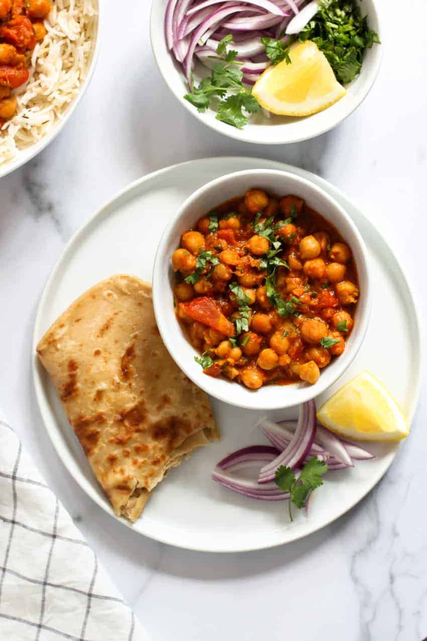 chickpea curry served with homemade parathas, lemon wedge and sliced onions