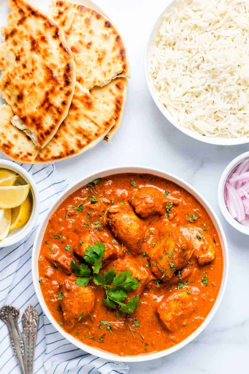 chicken tikka masala in a white bowl alongside naan and jeera rice.