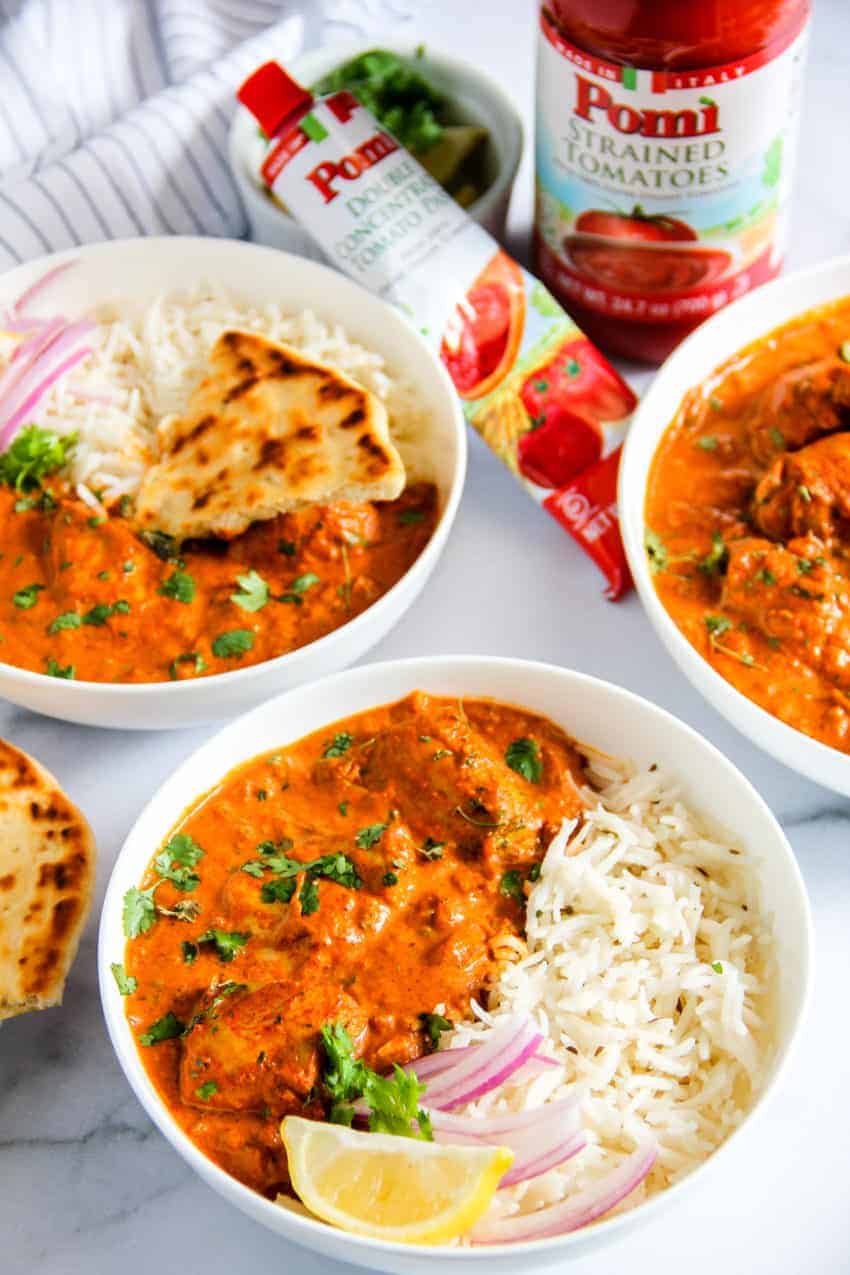 chicken tikka masala served in 3 white bowls along with basmati rice and naan 