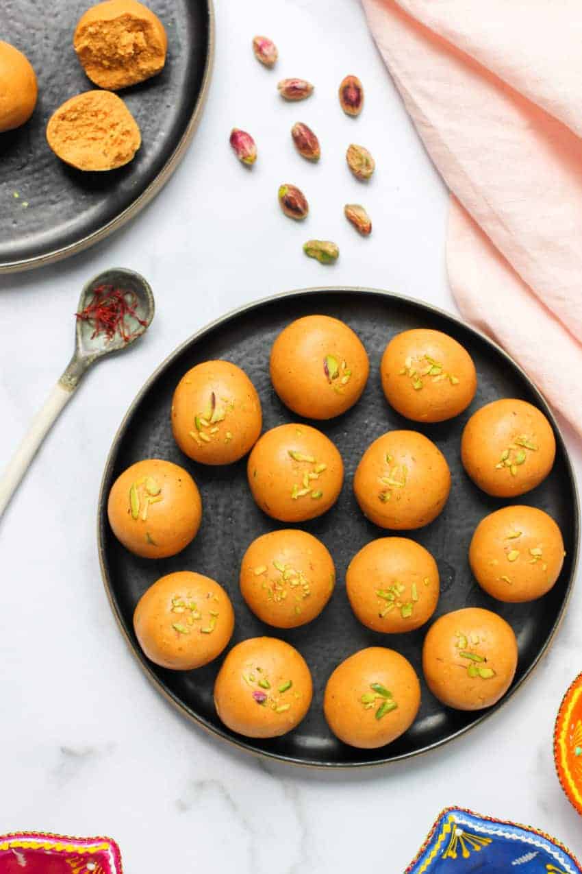 Besan Ladoo in a black plate with saffron and pistachios on the side