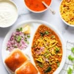 Misal Pav served in a white plate with all the garnish ingredients on the sides