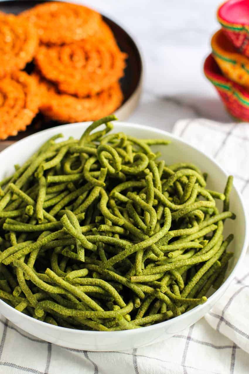 Spinach Sev in a white bowl with Chakli in the background 