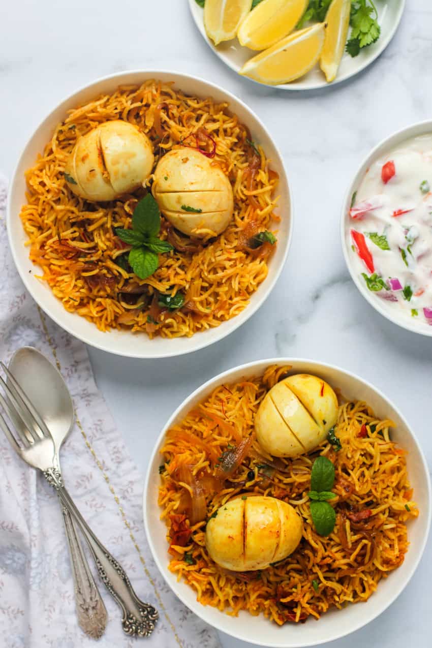 Egg Biryani served in 2 white bowls with raita on the side