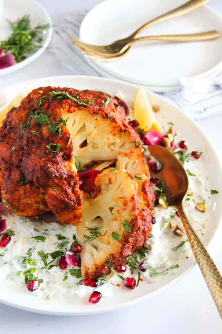 whole tandoori cauliflower served with cucumber raita in a white plate 
