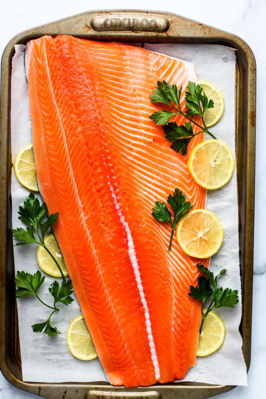 Raw salmon on a baking tray with lemon and parsley 