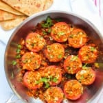 stuffed tomatoes in a frying pan with parathas on the side