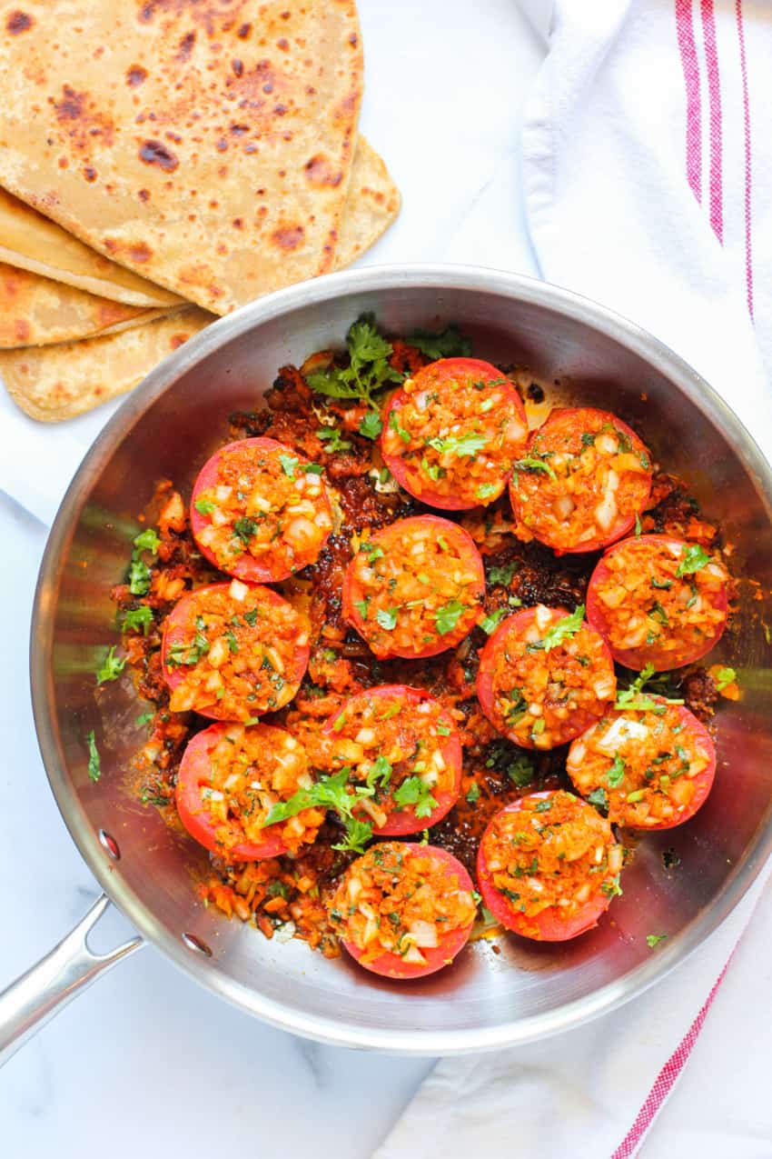 Stuffed tomatoes in a frying pan with parathas on the side 