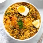 chicken biryani in a white bowl with half boiled egg on top