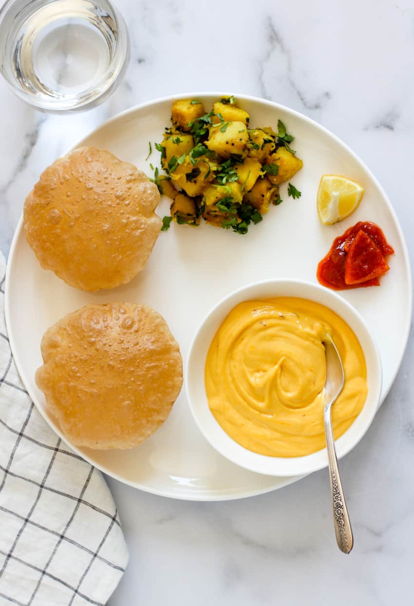 Shrikhand, puri and batat bhaji served in a white plate