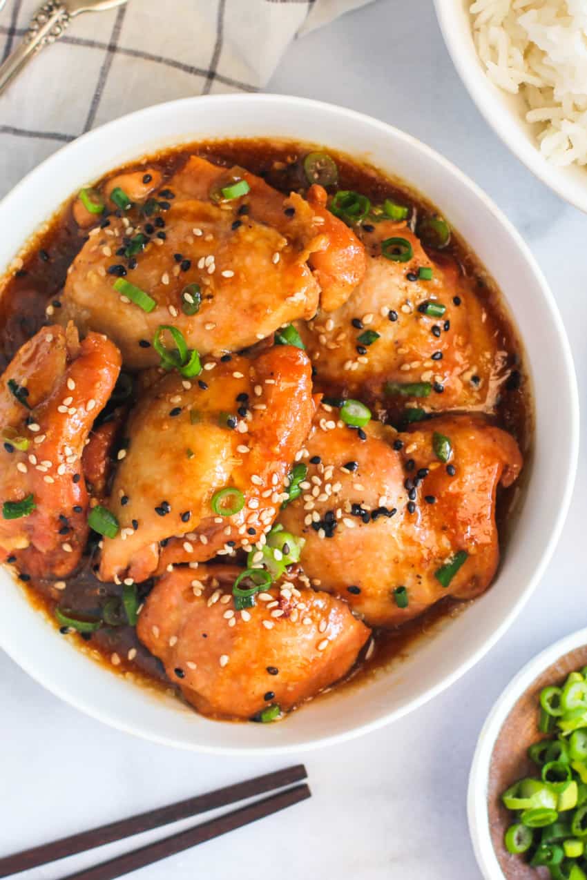 Chicken garnished with sesame seed and scallions served in a white bowl 