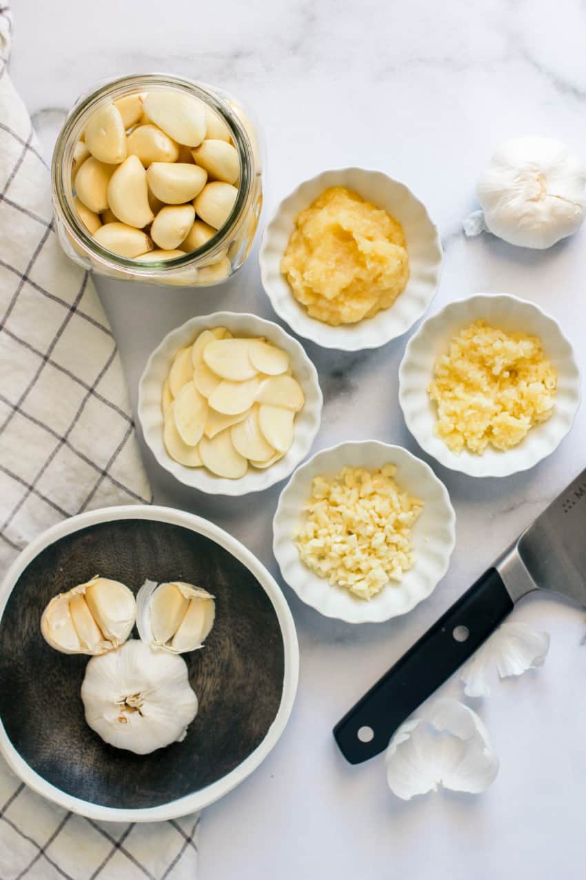 peeled fresh garlic in jar with chopped and sliced garlic in bowls 