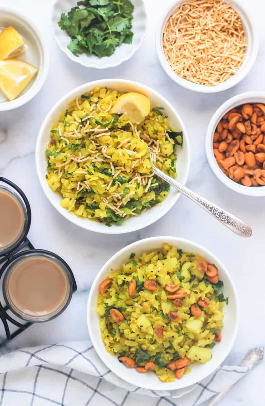 Poha served in white bowls with tea and toppings on the side