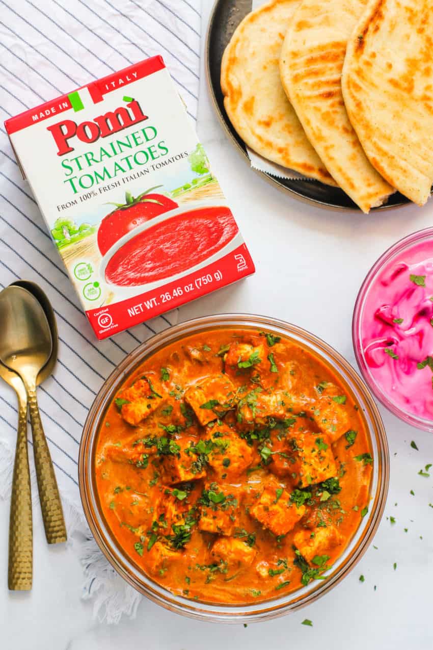 paneer butter masala with naan and raita with a box of tomatoes next.  